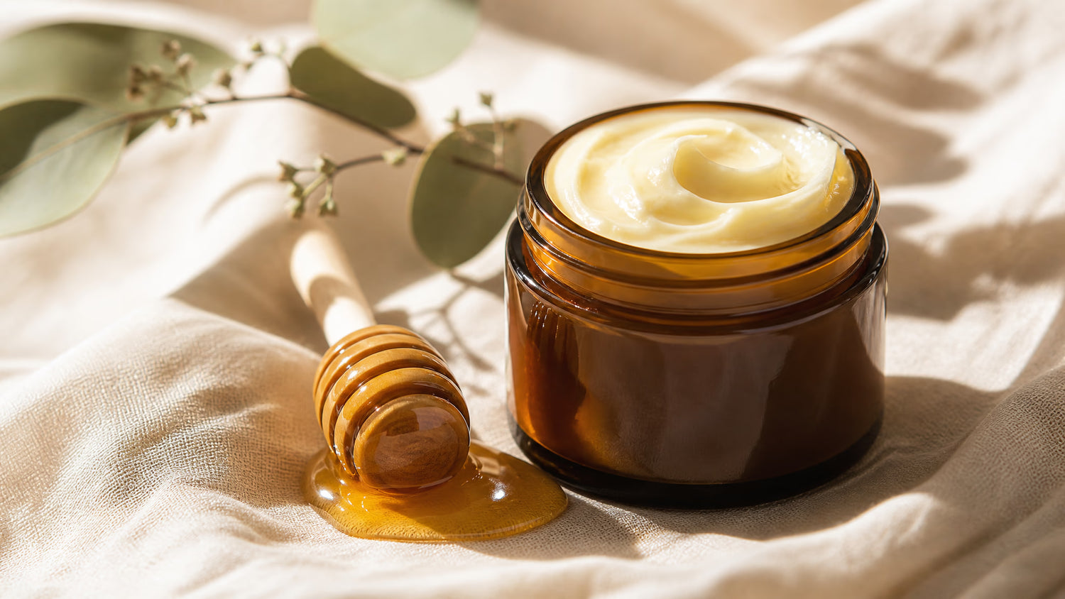 Jar of beef tallow and honey balm on beige linen with raw honey dipper